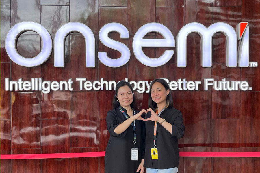 Two ladies standing by the onsemi logo, forming a heart shape with their hands.