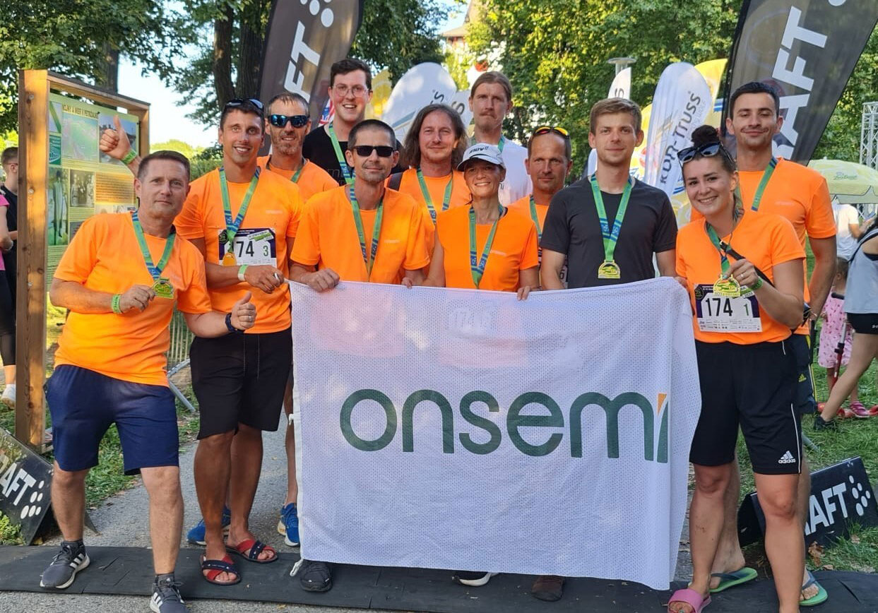 onsemi employees from Slovakia at a running race, standing by an onsemi sign and smiling.